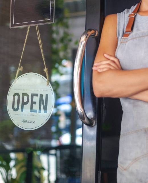The woman is a waitress in an apron, the owner of the cafe stand The woman is a waitress in an apron, the owner of the cafe stands at the door with a sign Open waiting for customers. Small business concept, cafes and restaurants